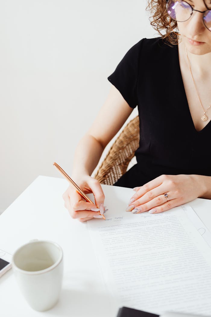 A woman writing on a document with a pen at a white desk, conveying focus and professionalism.